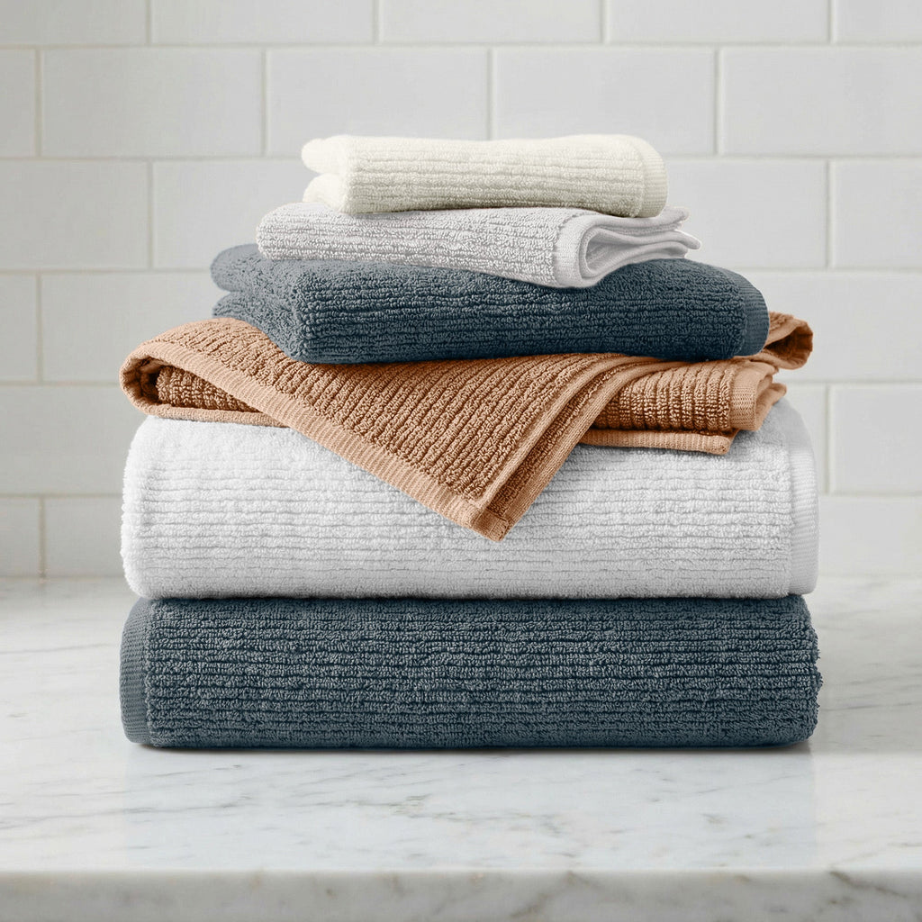 Stack of folded towels in various colors on a marble surface with a tiled wall background